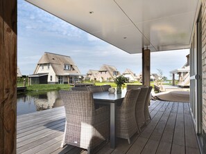A covered outdoor area with wicker furniture, a table, and a view of traditional houses by a body of water. - Spacious Villa With a Sauna, at the Tjeukemeer (Delfstrahuizen)