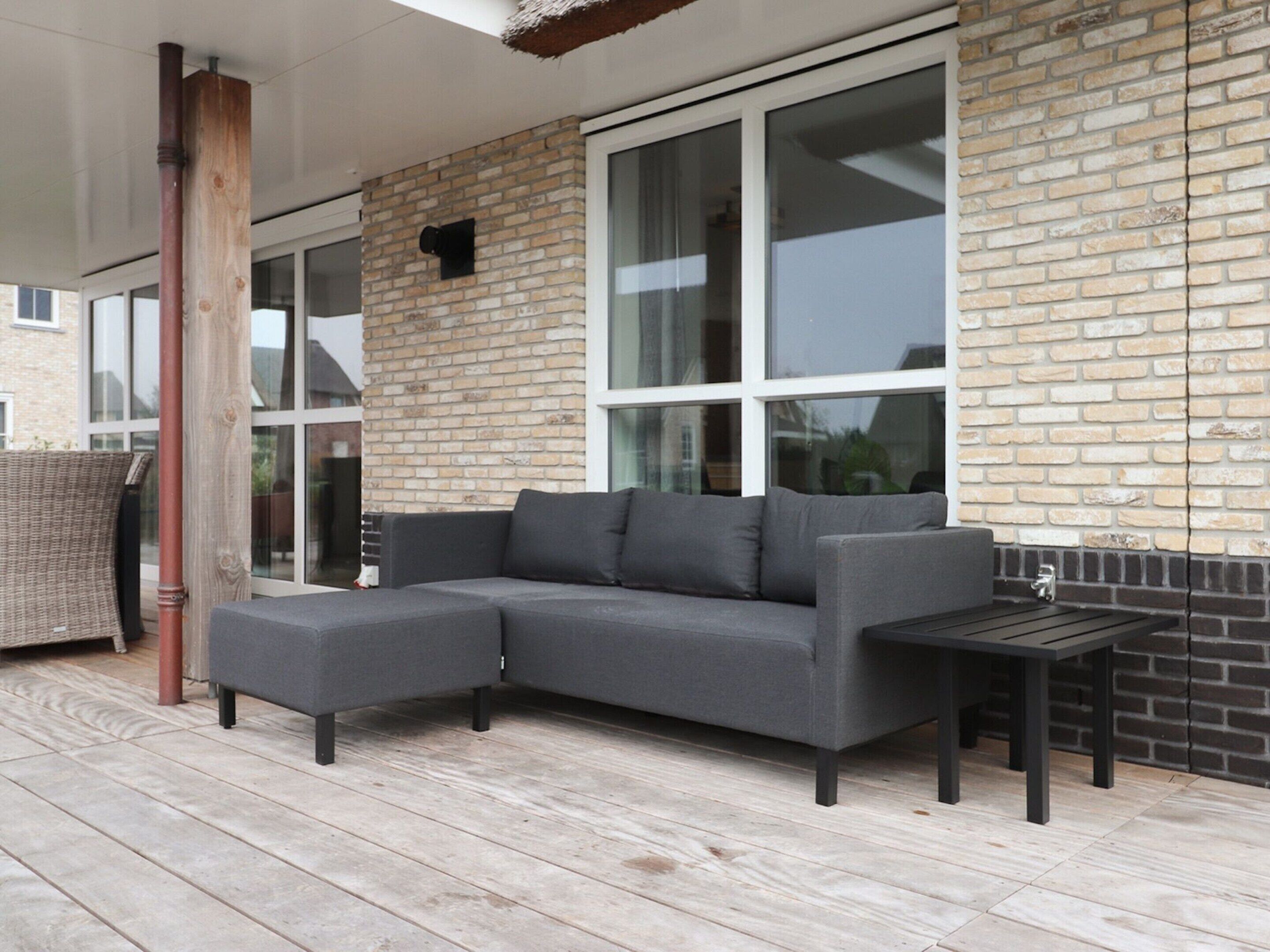 A covered outdoor area with a grey sectional sofa, a small table, and a wicker chair.