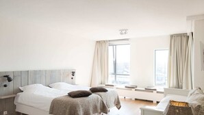 A bedroom with two beds, a bedside table, a lamp, and a window with curtains. - Modern Apartment in The Hague (The Hague)