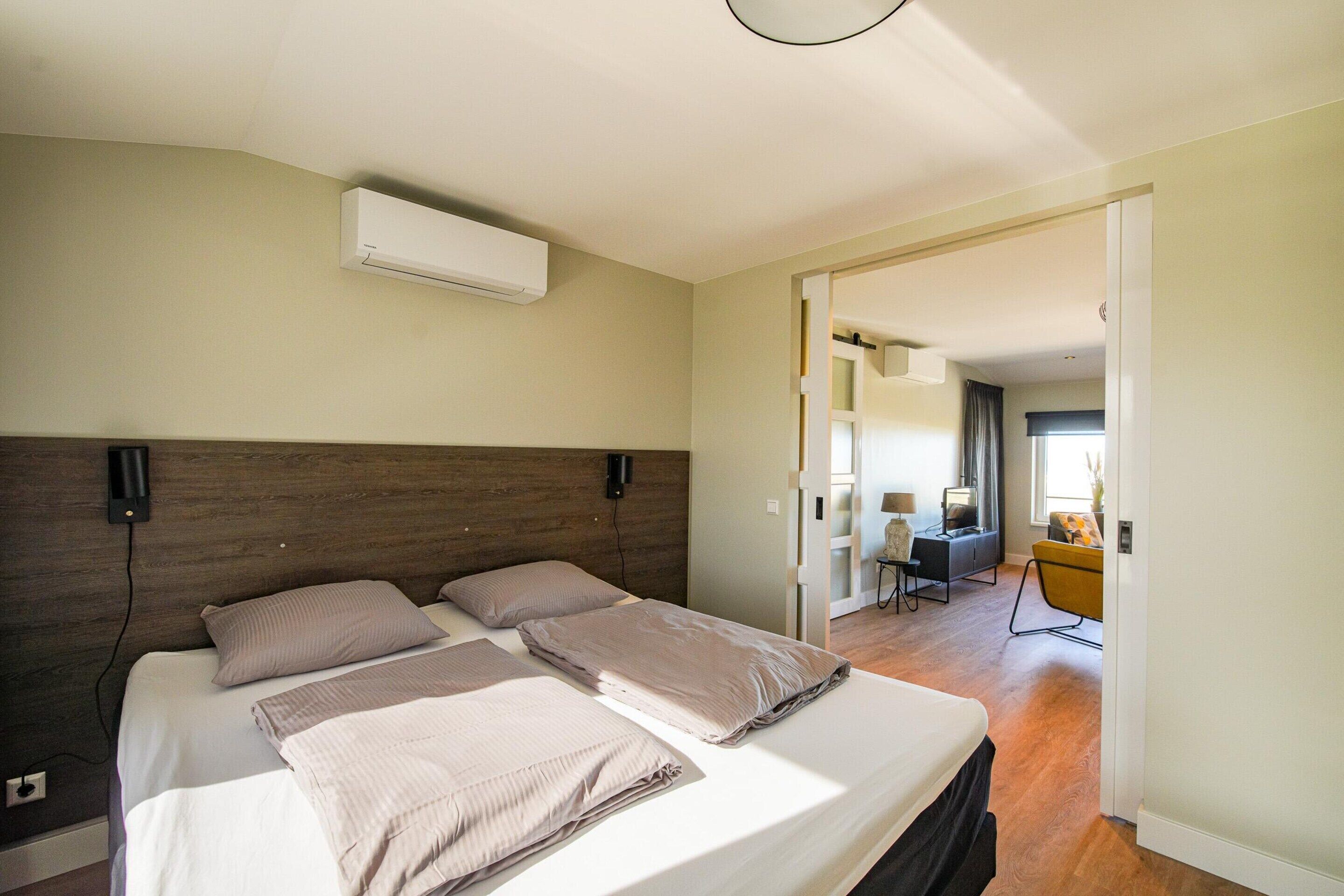 A bedroom with a bed, an air conditioner, and a desk with a chair.