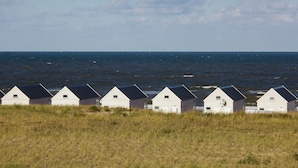 Eine Reihe weißer Strandhäuser mit dunklen Dächern vor dem Hintergrund des Ozeans und eines klaren Himmels.