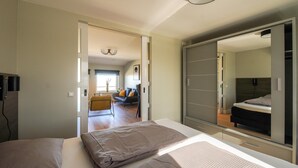 Ein modernes Schlafzimmer mit einem großen Bett, einem Kleiderschrank und Blick in den Wohnbereich.