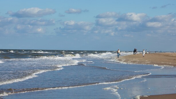 Ein Strand mit Wellen, einem klaren Himmel und Menschen, die spazieren gehen.