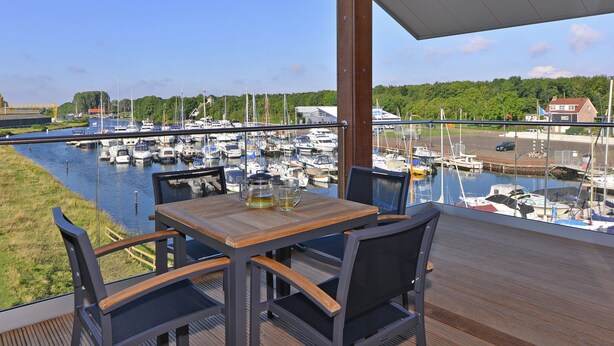 Ein Balkon mit Holztisch und -stühlen mit Blick auf einen Yachthafen und Boote.