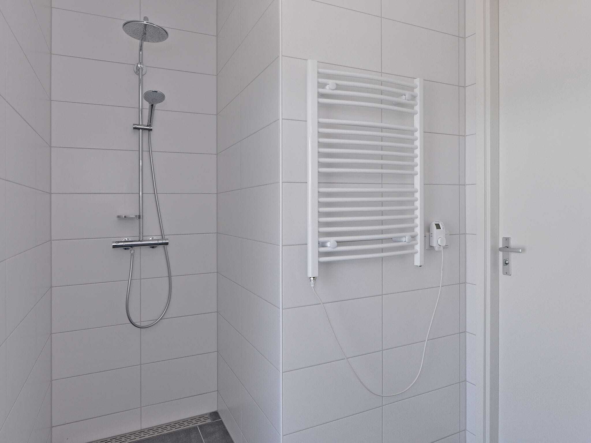 A bathroom with a shower, a white towel rack, and a door with a handle.