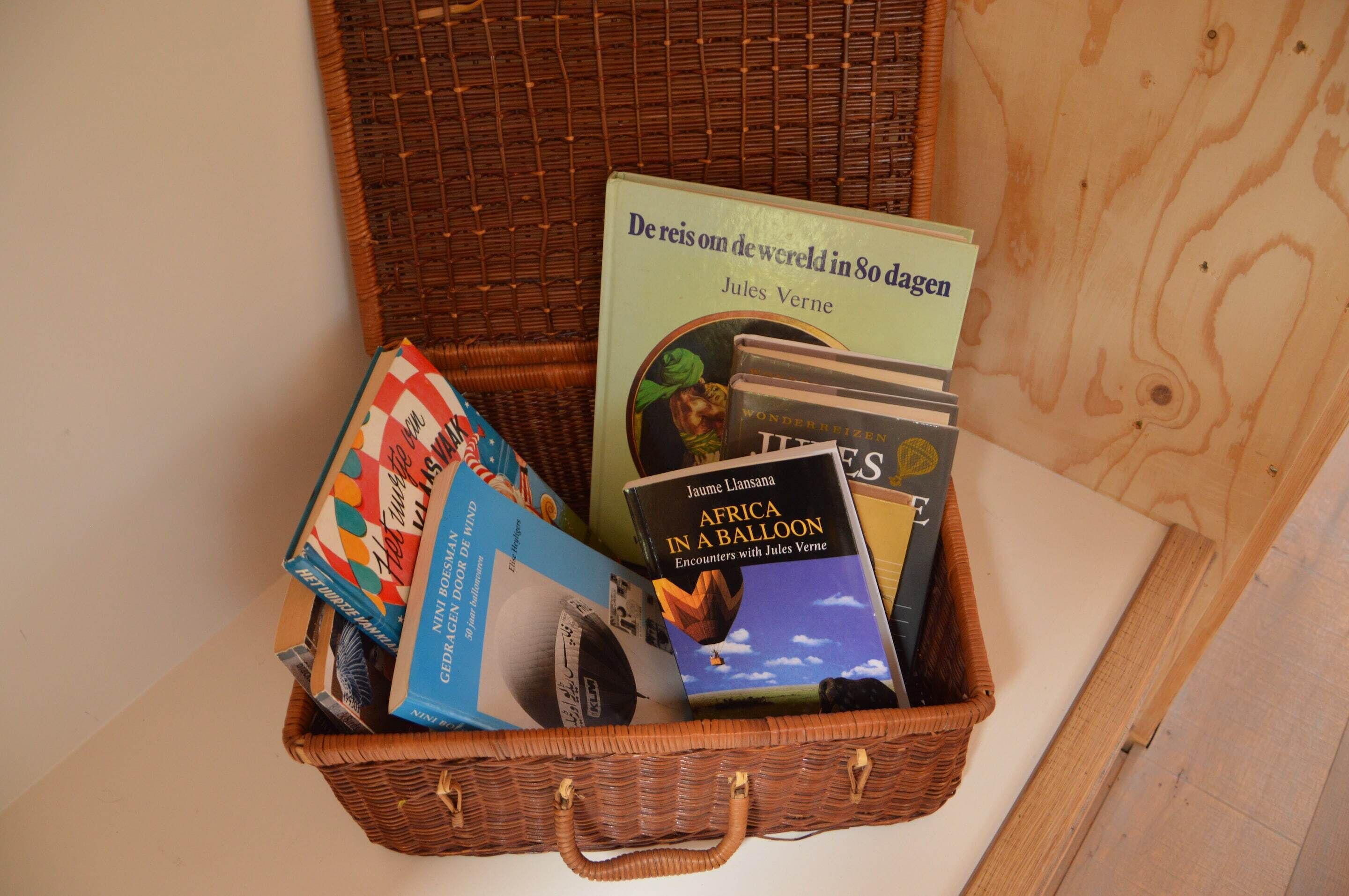 A wicker basket containing books, including 'Africa in a Balloon' by Jules Verne.