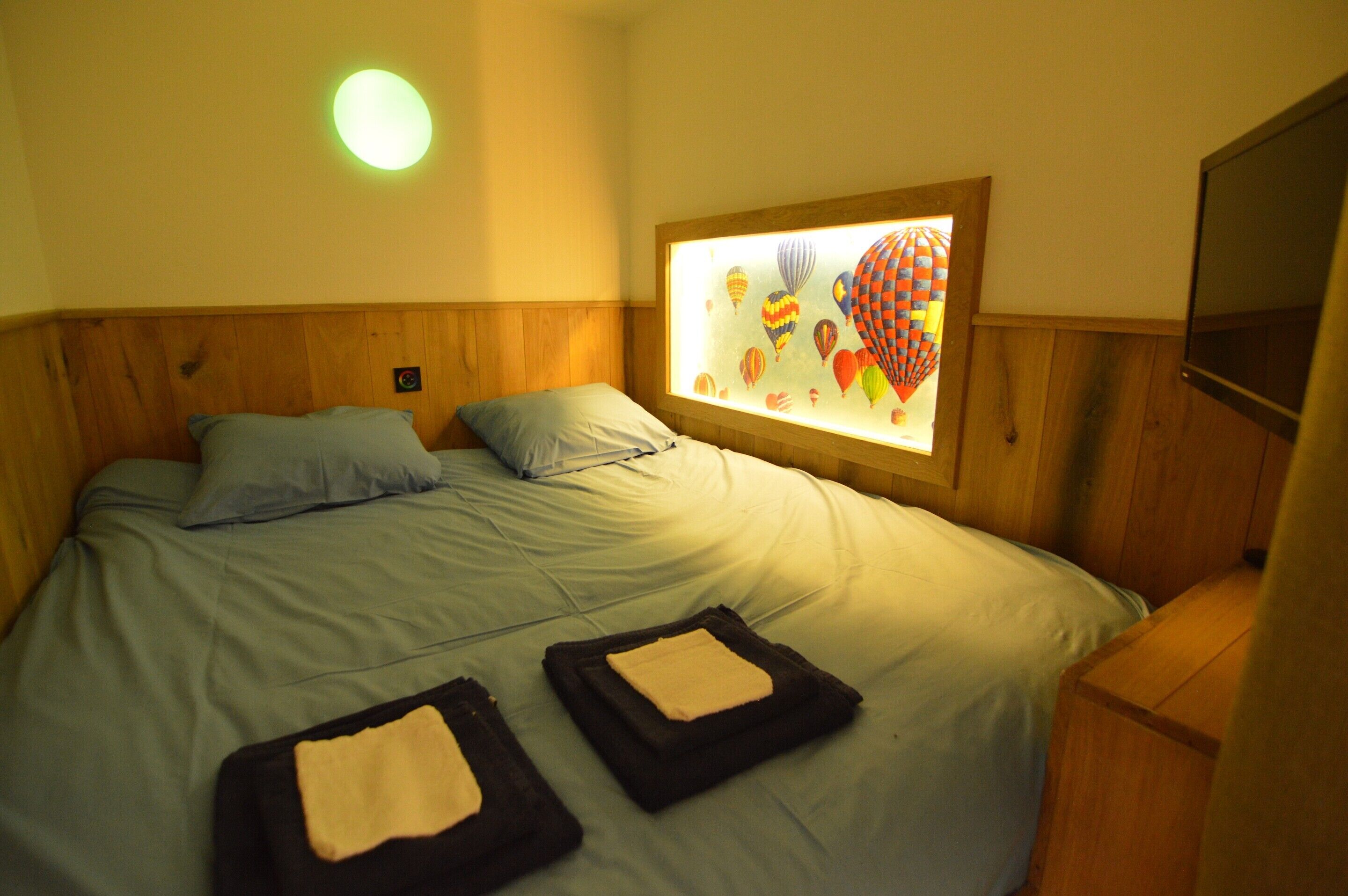 A bed with a wooden headboard, two pillows, and a wall-mounted TV.