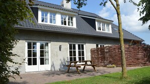 A two-story house with a brick exterior, large windows, and a wooden picnic table in front. - Holiday Home in Haaren Near De Efteling (Haaren)