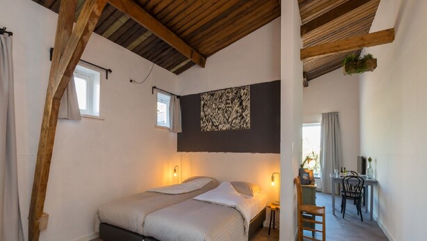 A bedroom with a large bed, wooden beams, a small table with chairs, and a hanging plant. - Apartment in Koudekerke Near Seabeach (Koudekerke)