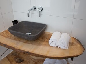A bathroom with a stone sink, two rolled towels, and a wooden vanity. - Apartment in Koudekerke Near Seabeach (Koudekerke)