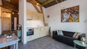 A modern kitchen with wooden beams, a dining area with a table and chairs, and a living room with a sofa and a painting on the wall. - Apartment in Koudekerke Near Seabeach (Koudekerke)