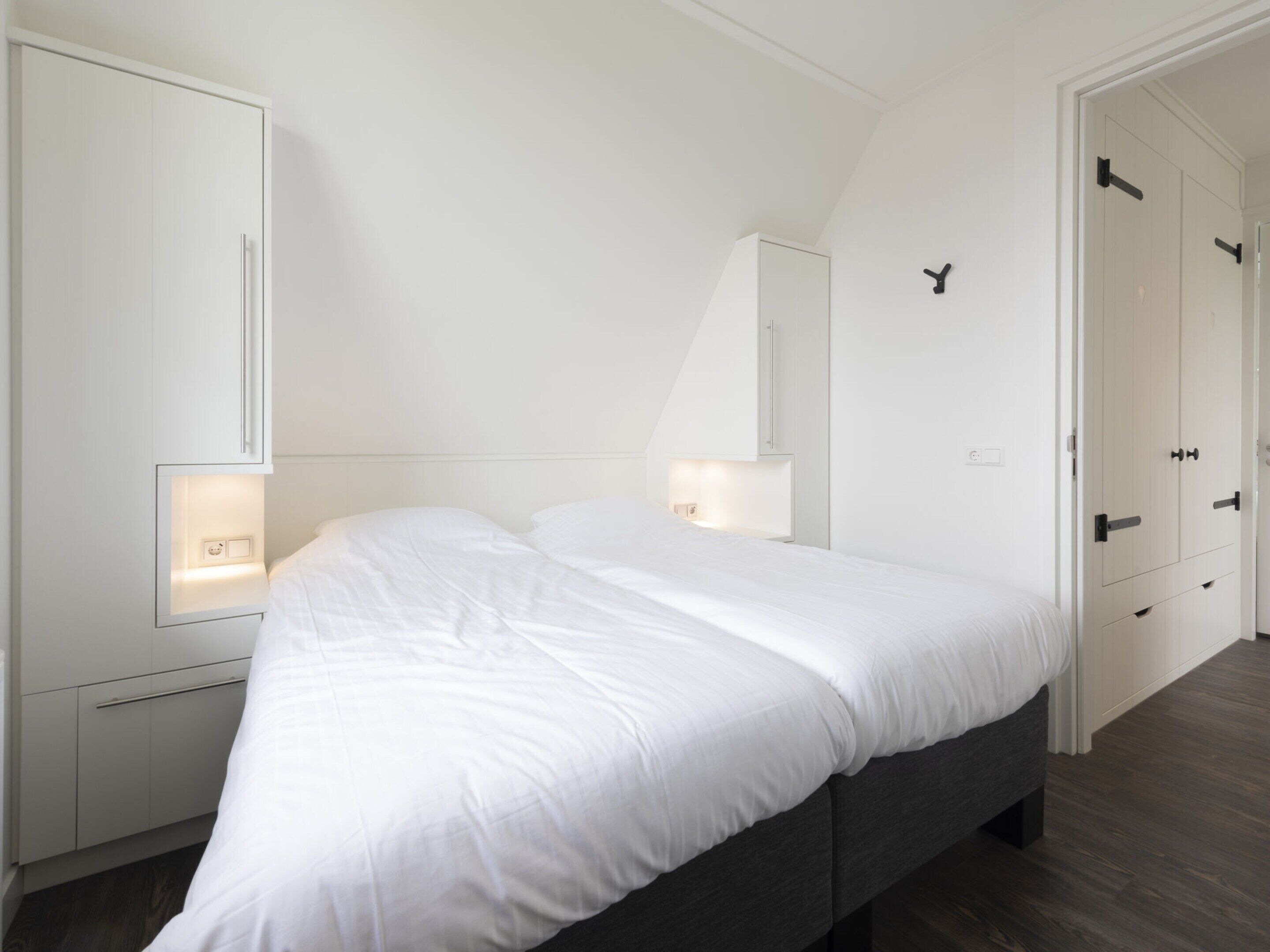 A bedroom with a large bed, white walls, and built-in wardrobes.