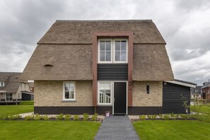 Een modern huis met rieten dak, een zwarte deur en een gevel van baksteen.