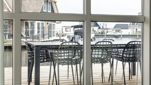 A view from a window overlooking a dock with a table and chairs, a canal, and buildings in the background. - Villa With a Sauna in Tjeukemeer (Delfstrahuizen)