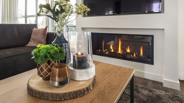 A modern living room with a fireplace, a sofa, and decorative items on a wooden coffee table. - Villa With a Sauna in Tjeukemeer (Delfstrahuizen)