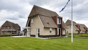 A row of modern houses with pitched roofs, a flagpole, and a well-maintained lawn. - Villa With a Sauna in Tjeukemeer (Delfstrahuizen)