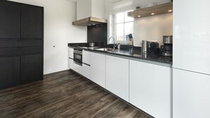 A modern kitchen with dark wood flooring, white cabinetry, and stainless steel appliances. - Villa With a Sauna in Tjeukemeer (Delfstrahuizen)