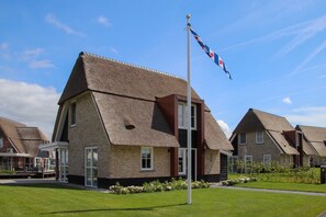 A residential building with a thatched roof, a flagpole with a flag, and a well-maintained lawn. - Villa With a Sauna in Tjeukemeer (Delfstrahuizen)