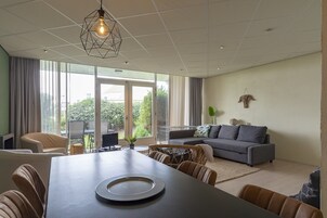 Una sala de estar moderna con una mesa de comedor, sofá y ventanas amplias que dan a zonas verdes.