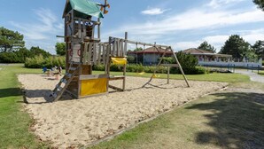 A playground with a wooden play structure, including a slide and climbing area, set in a sandy area with grass and trees around. - Nice Apartment With Garden Near the North Sea (Julianadorp)
