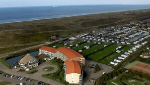 An aerial view of a coastal area with a large building featuring a curved roof, a parking lot, and a marina. - Nice Apartment With Garden Near the North Sea (Julianadorp)