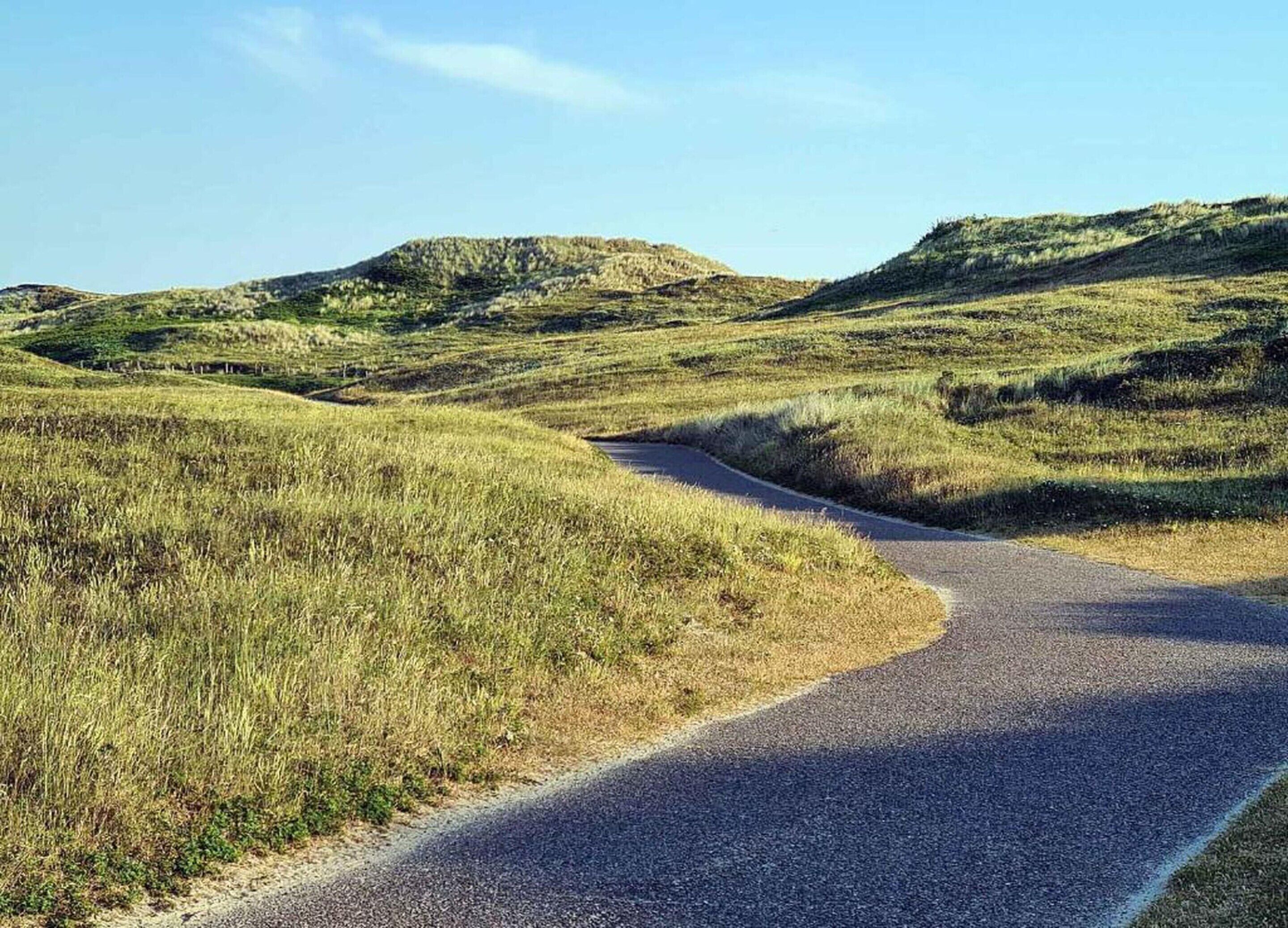 A winding road through a grassy landscape with rolling hills.