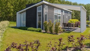 Uma casa moderna com uma grande janela de vidro, um pátio com móveis de exterior e um jardim bem cuidado.