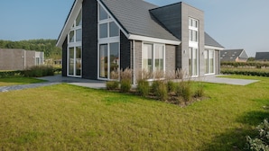 Une maison moderne à deux étages, dotée de grandes fenêtres, d’un toit en pente et d’une pelouse bien entretenue.