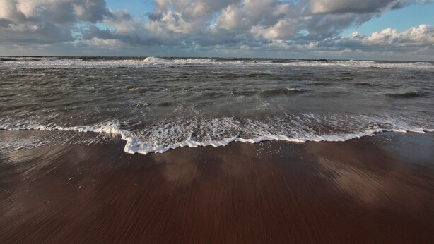 A beach with waves and a cloudy sky.