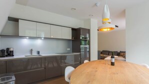 A modern kitchen with a wooden dining table, white cabinets, and a hanging light fixture.