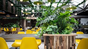 A modern indoor dining area with yellow chairs, a wooden planter with green plants, and hanging lights. - Villa With med Children's Room in Limburg (Roggel)