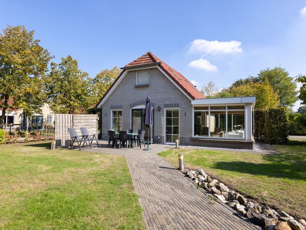 A two-story house with a brick exterior, a tiled roof, and a covered patio area with outdoor furniture. - Cosy Holiday Home in Twente (Hoge Hexel)