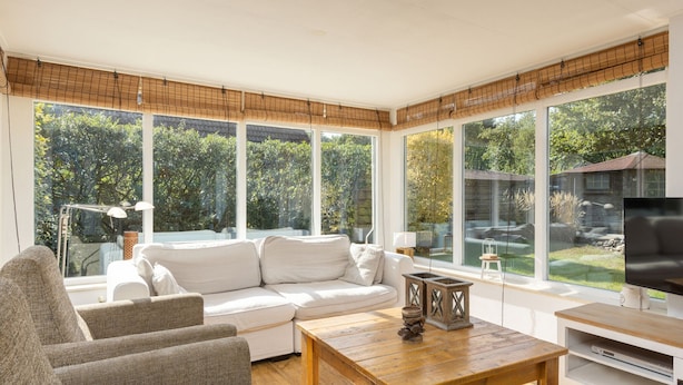 A modern living room with a white sofa, a wooden coffee table, and a television on a white stand. Large windows provide a view of the outdoors. - Cosy Holiday Home in Twente (Hoge Hexel)