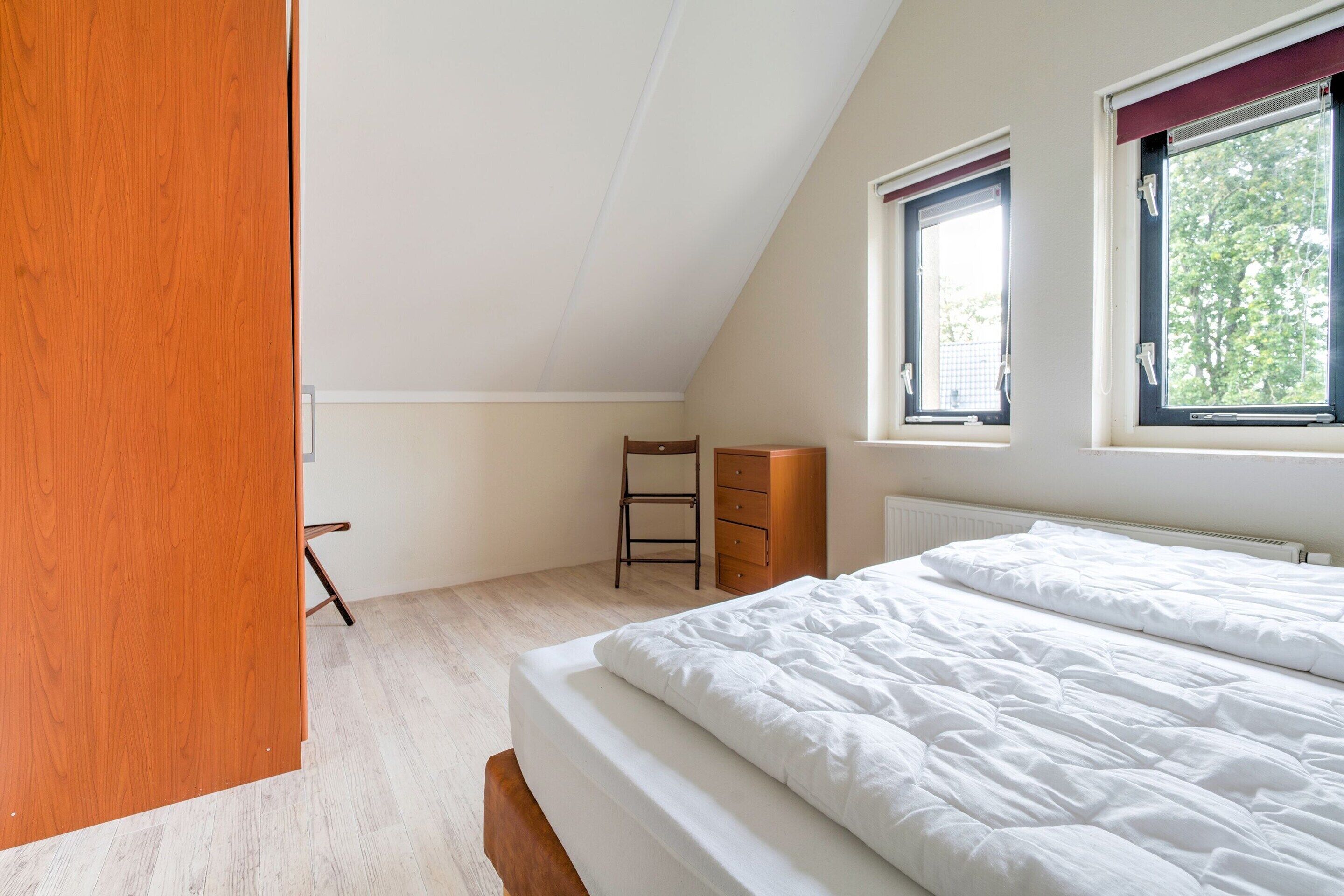 A bedroom with a bed, a wooden wardrobe, a chair, and a radiator.