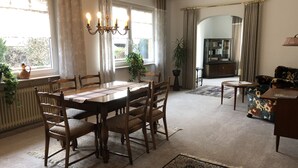 A dining area with a wooden table and chairs, a chandelier, and a view of the outdoors through large windows. - Vacation apartment "Zum Wiesenblick" in the heath village of Eimke, 130 sqm  (Eimke)