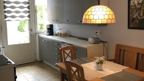 A compact kitchen with grey cabinets, a wooden dining table with chairs, a hanging lamp, and a window with blinds. - Vacation apartment "Zum Wiesenblick" in the heath village of Eimke, 130 sqm  (Eimke)