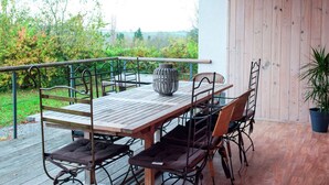 An outdoor patio with a wooden table and chairs, a metal railing, and a potted plant. - A Superb Cottage in the Middle of a Natural Park (Hotton)