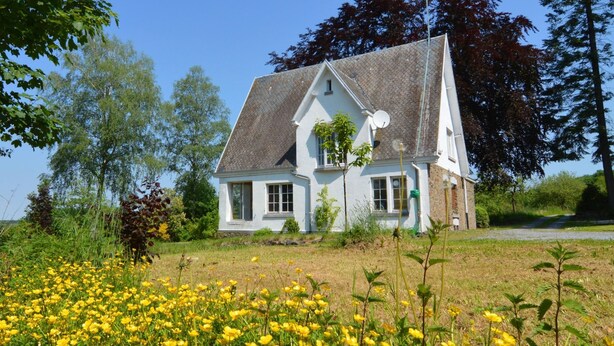 A white house with a steep roof, surrounded by a field of yellow flowers and trees. - A Superb Cottage in the Middle of a Natural Park (Hotton)