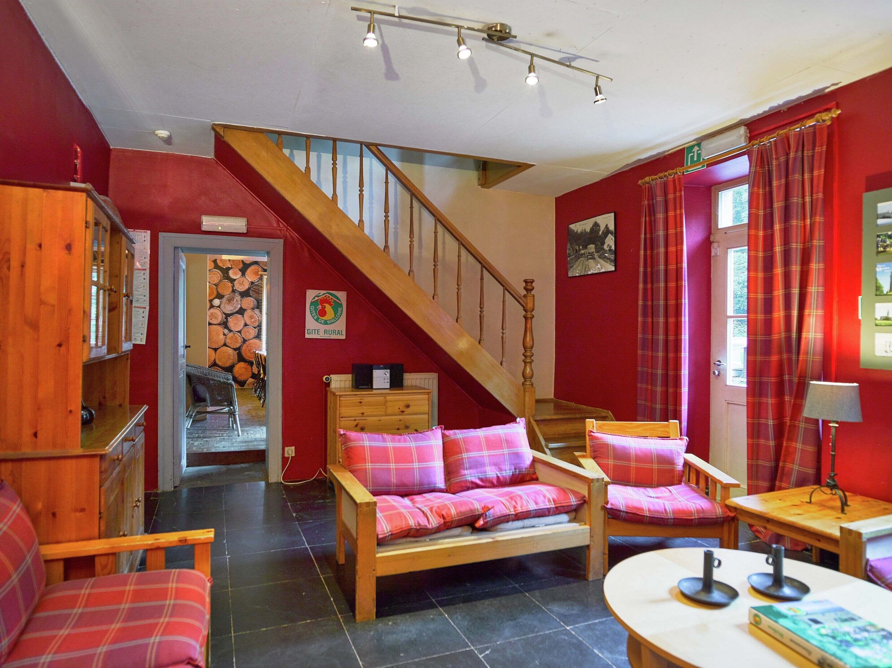 A cozy room with a wooden bed, a wooden chair, a table with books, a staircase, and a red wall.