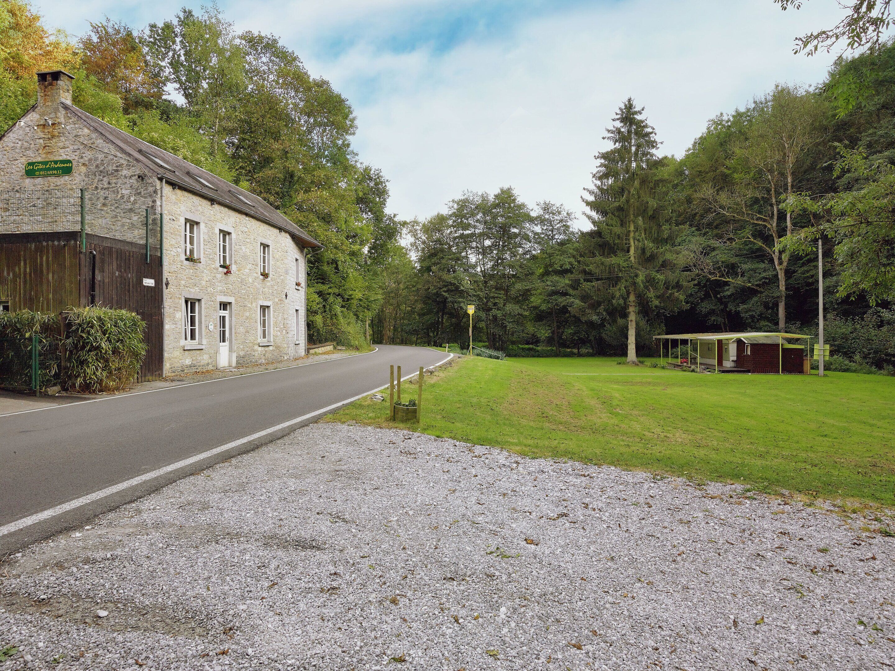 A stone building with a gravel driveway, a covered outdoor area, and a forested backdrop.