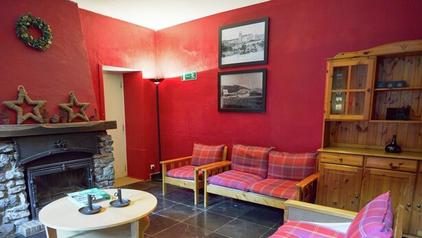 A red-walled room with a fireplace, a sofa with plaid cushions, a wooden cabinet, and two framed pictures on the wall. - Spacious Family Home, Sosoye (Anhée)