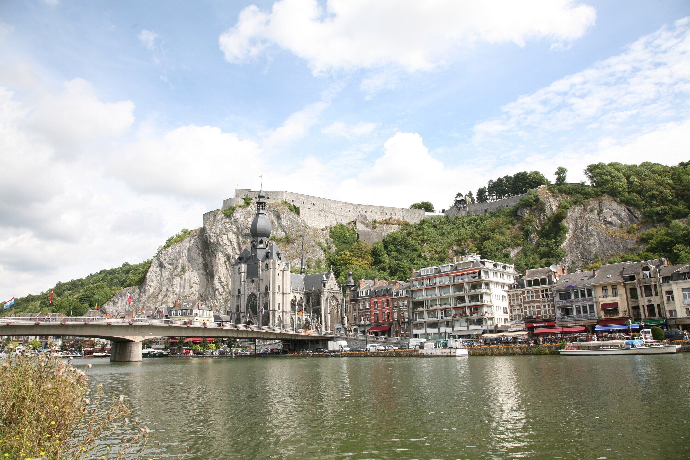 A historic building with a large bell tower, a bridge, and a river with boats.