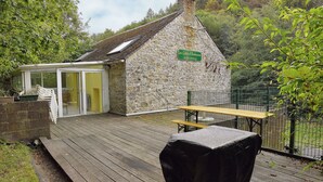 A stone building with a green sign, a wooden deck, and a fenced garden area. - Spacious Family Home, Sosoye (Anhée)