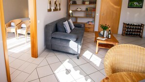 Un salón con un sofá gris, una mesa de centro de madera, una silla de mimbre, una estantería y un mueble para vinos.