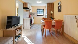 Un espacio habitable compacto con kitchenette, comedor y televisor sobre un soporte de madera.