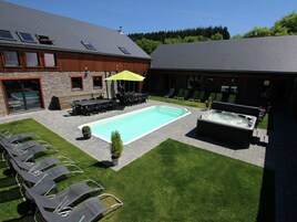 Un patio trasero con piscina, sillas de descanso, jacuzzi y mobiliario para exteriores.