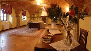 A spacious room with a high arched brick ceiling, a fireplace, a sofa, a dining table with a vase of flowers, and a large window with curtains. - Mansion in Nizza Monferrato With Pool & Views (Nizza Monferrato)