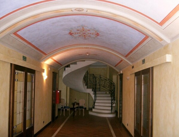 A grand hallway with a curved ceiling, a spiral staircase, and a small seating area with chairs and a table. - Mansion in Nizza Monferrato With Pool & Views (Nizza Monferrato)