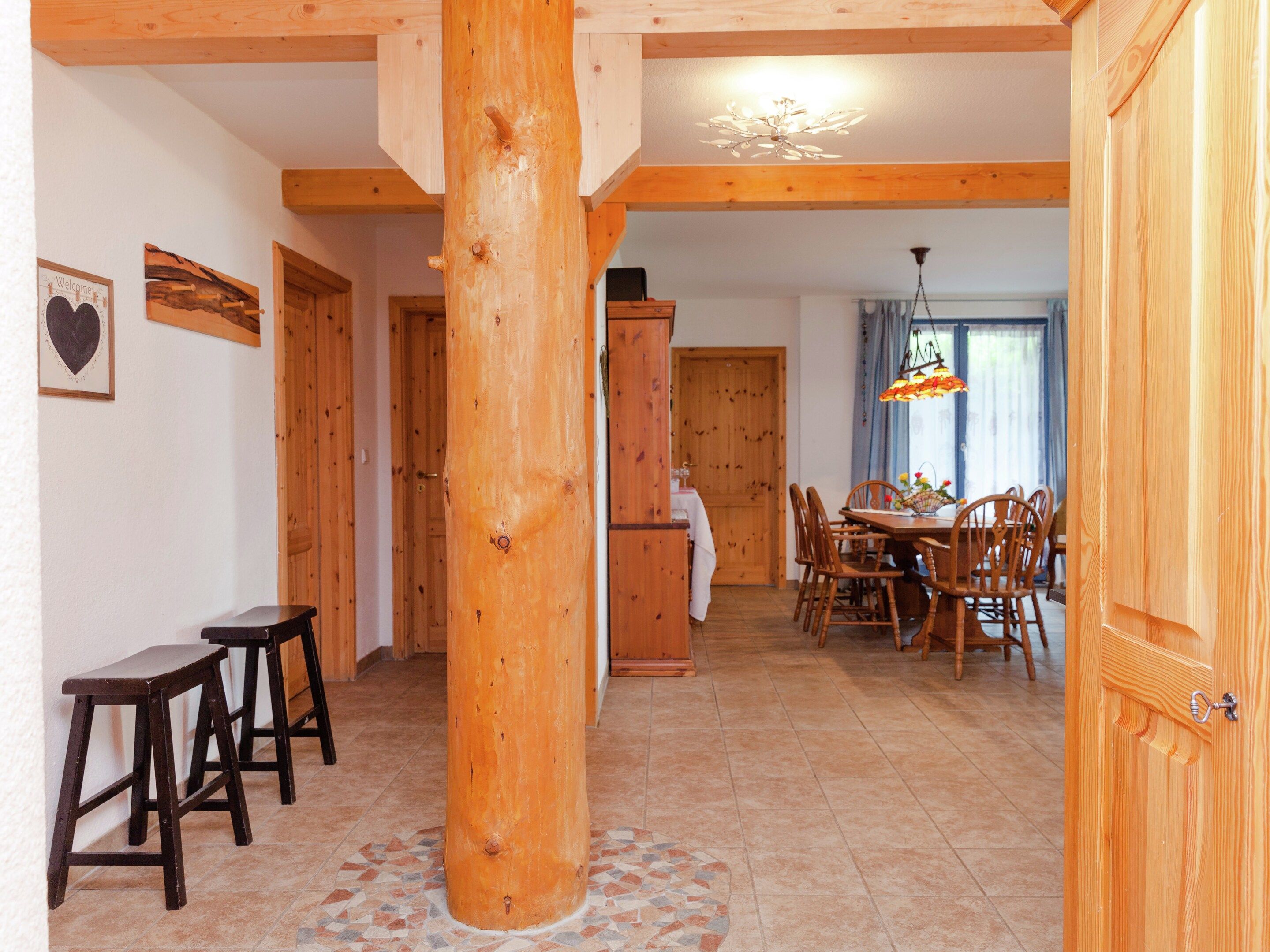 A wooden interior with a central column, a dining area with chairs and a table, and a kitchen area with cabinets.