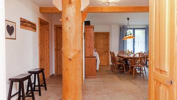 A wooden interior with a central column, a dining area with chairs and a table, and a kitchen area with cabinets.